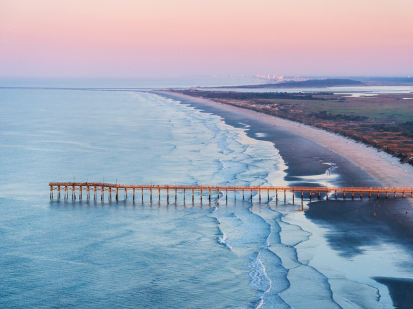 Aerial sunrise view of the wooden fishing pier extending into the Atlantic Ocean at Sunset Beach.